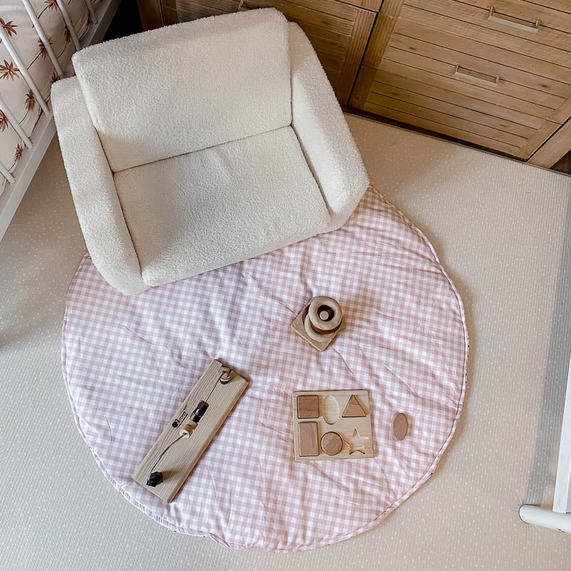 A top view of Snuggly Jacks Peachy Pink Gingham Playmat set in a modern nursery with scattered wooden toys