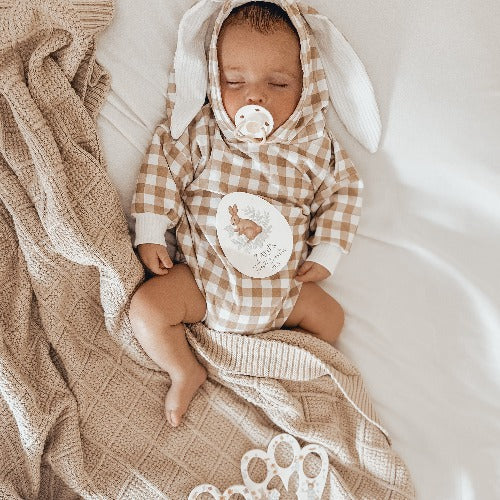 Newborn baby laying on a bed with a bunny outfit and snuggly jacks organic taupe knitted blanket