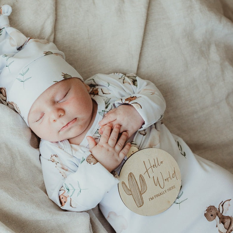 A baby sleeping on a cotton sheet with an announcment disc announcing hello world