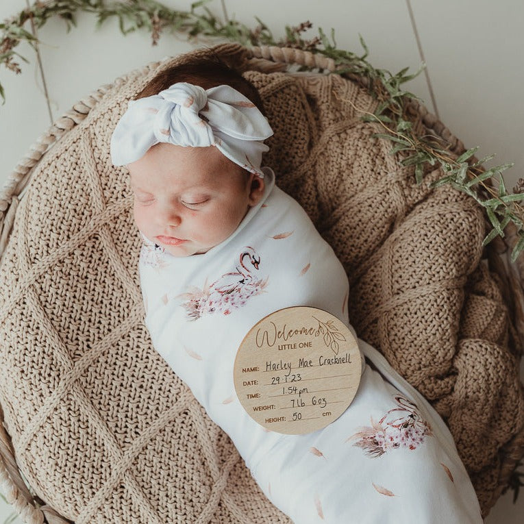 Bright white light cascading in on a cute baby swaddled and laying on a soft cotton knitted blanket using an announcement disk to show when she was born.