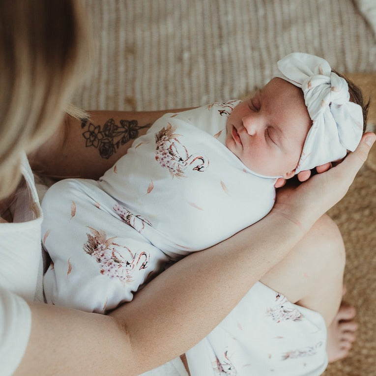 Close up of a sleeping baby wearing a jersey top knot and wrapped in a swaddle being held by mum endearingly