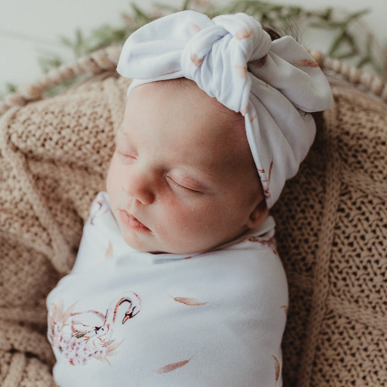 Baby wearing a swan jersey top knot and swaddled in a snuggly jacks stretch wrap