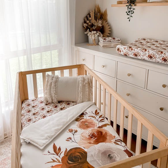 Wide shot of a nursery with fitted crib sheets, burp cloths, change mat covers and crib quilt all in a willow floral style print.